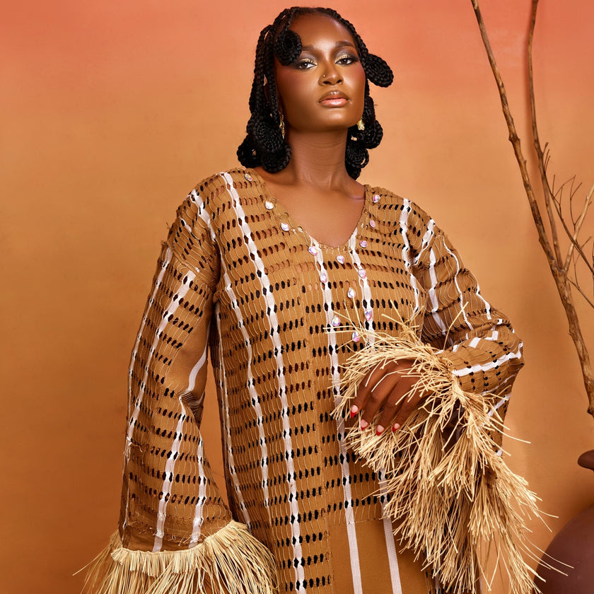 Front view: Model in the Asàkè heritage-inspired maxi dress made from handwoven Sayán Aso Oke, showing V-neckline with hand-placed stone embellishments, natural raffia trims, and regal silhouette.