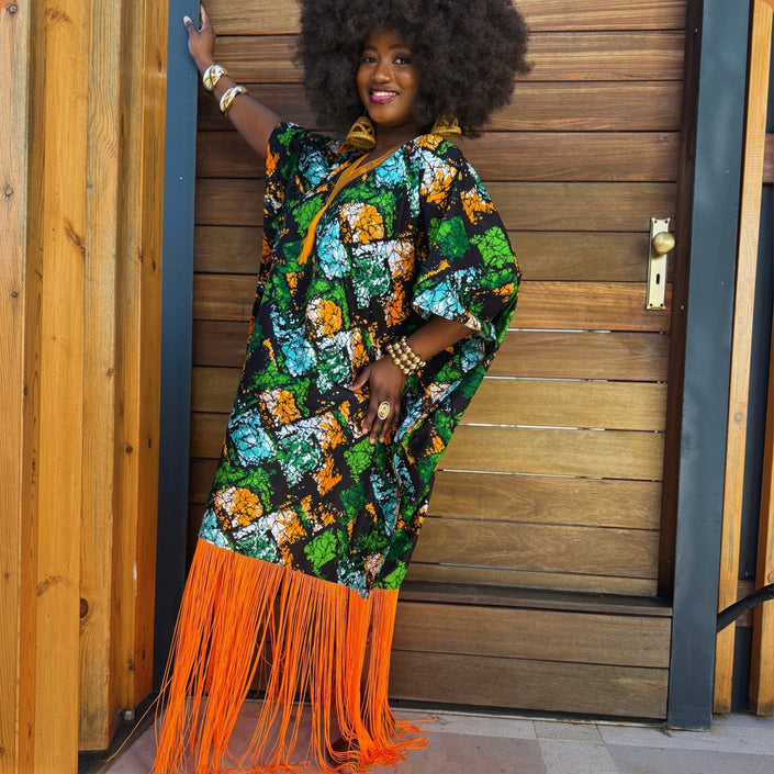 Side view of model wearing the Jọkẹ́ Bubu Dress: Side profile of model in the handmade oversized Ankara bubu maxi with vibrant multicolor print, hand-embroidered neckline, and dramatic orange tassel fringe showcasing its flowing relaxed fit.