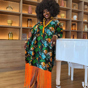 Front view of model wearing the Jọkẹ́ Bubu Dress: Model in a green, orange, black, and white Ankara maxi bubu dress with oversized flowing silhouette, embroidered V-neckline, and long orange tassel fringe hem, styled with deep side pockets for a relaxed fit.
