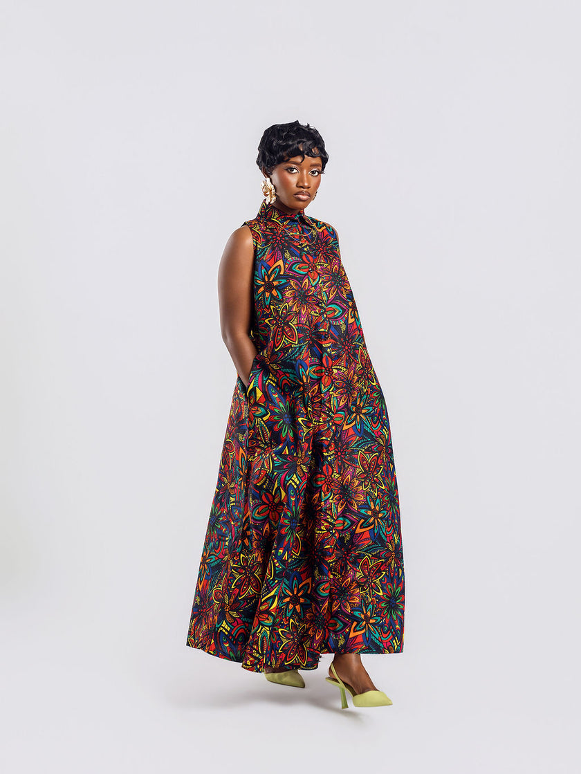 Full-length front view of a woman wearing the Amazin Apparels Kaleidoscope Gown, showing a large circular keyhole cutout and hidden elastic waistband in a vibrant floral African print.