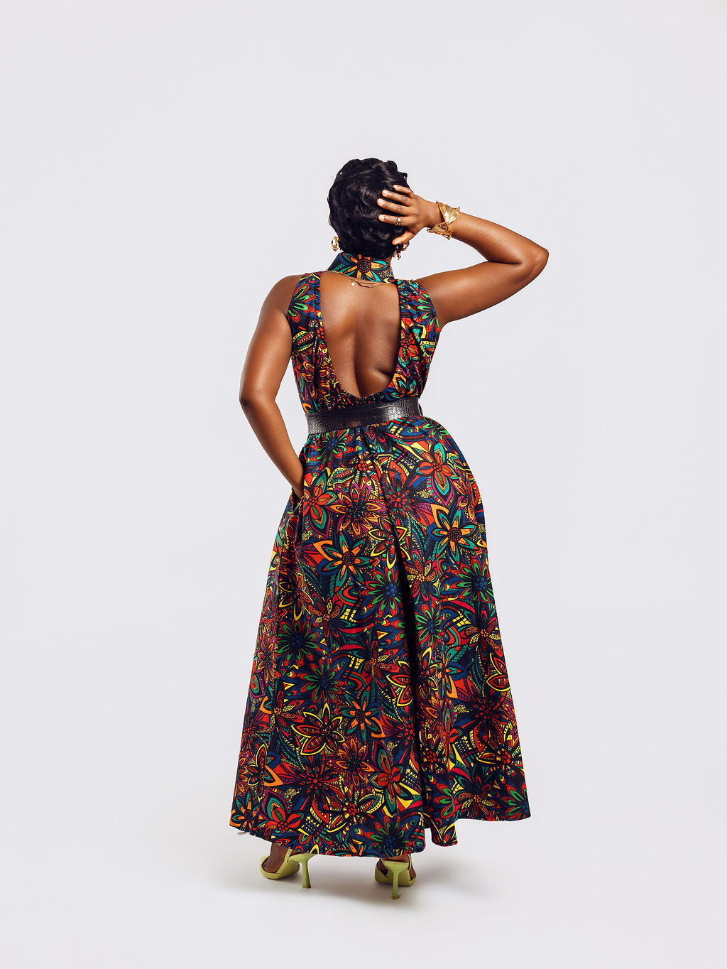 Full-length back view of a woman wearing the Amazin Apparels Kaleidoscope Gown, showing a large circular keyhole cutout and hidden elastic waistband in a vibrant floral African print.