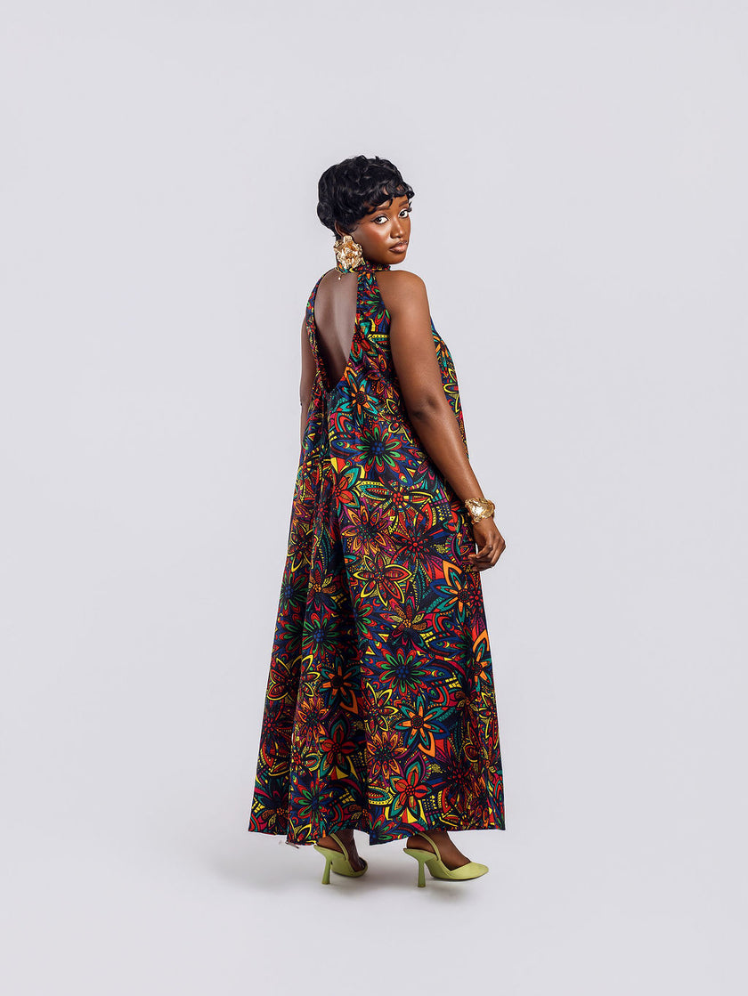 Full-length back view of a woman wearing the Amazin Apparels Kaleidoscope Gown, showing a large circular keyhole cutout and hidden elastic waistband in a vibrant floral African print.