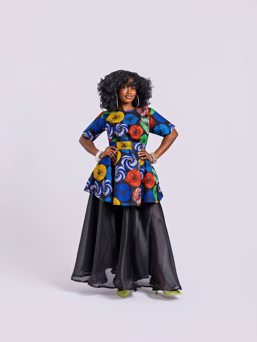A model wearing the two-piece set featuring a multi-colored swirl print peplum top and a sheer, unlined black organdy maxi skirt with two hidden pockets on both piece.