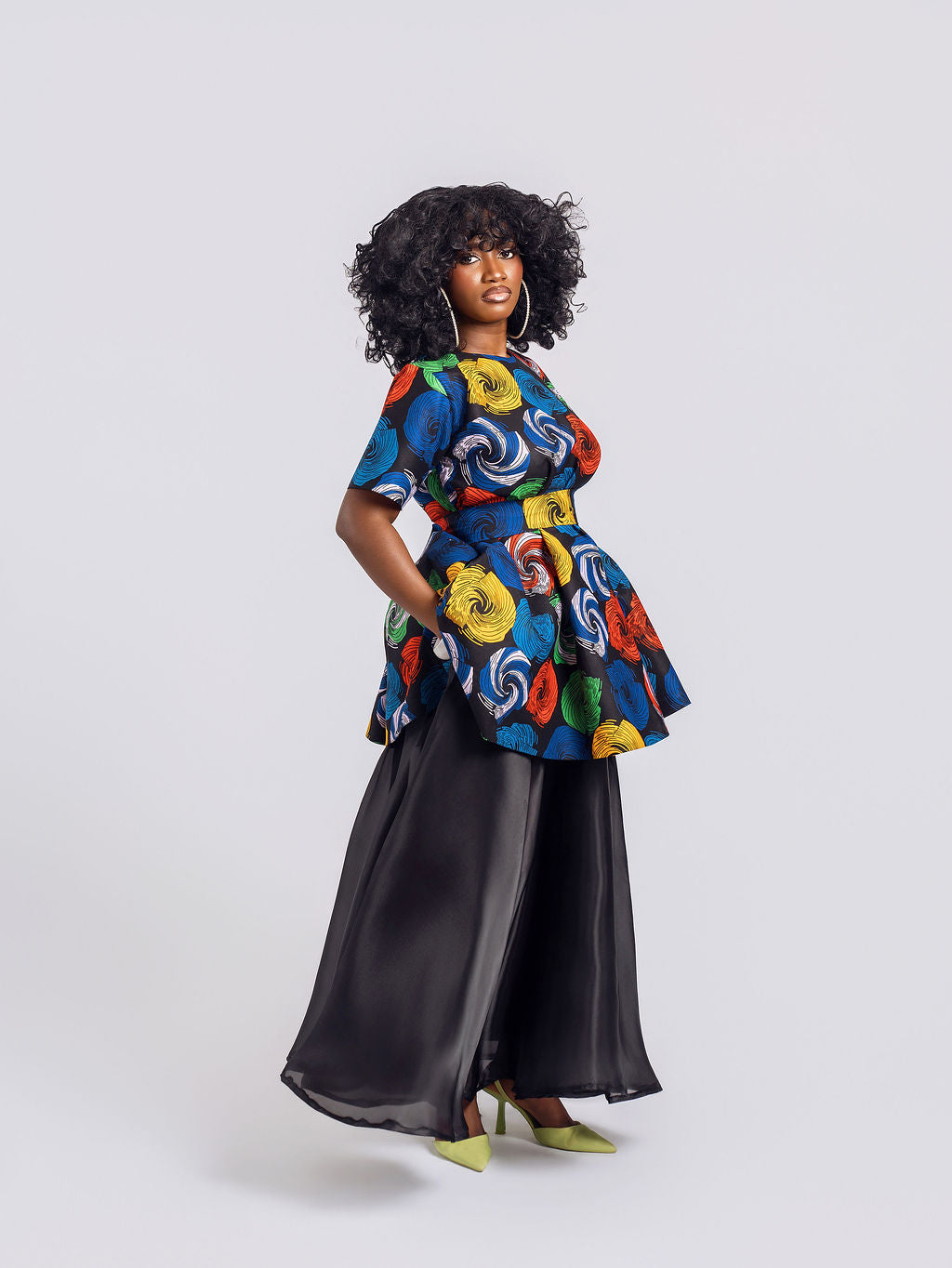 A model wearing the two-piece set featuring a multi-colored swirl print peplum top and a sheer, unlined black organdy maxi skirt