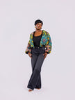 The front view of a cropped bomber jacket with a bold yellow and teal sunflower motif, with the front zip open, styled with high-waisted black jeans.