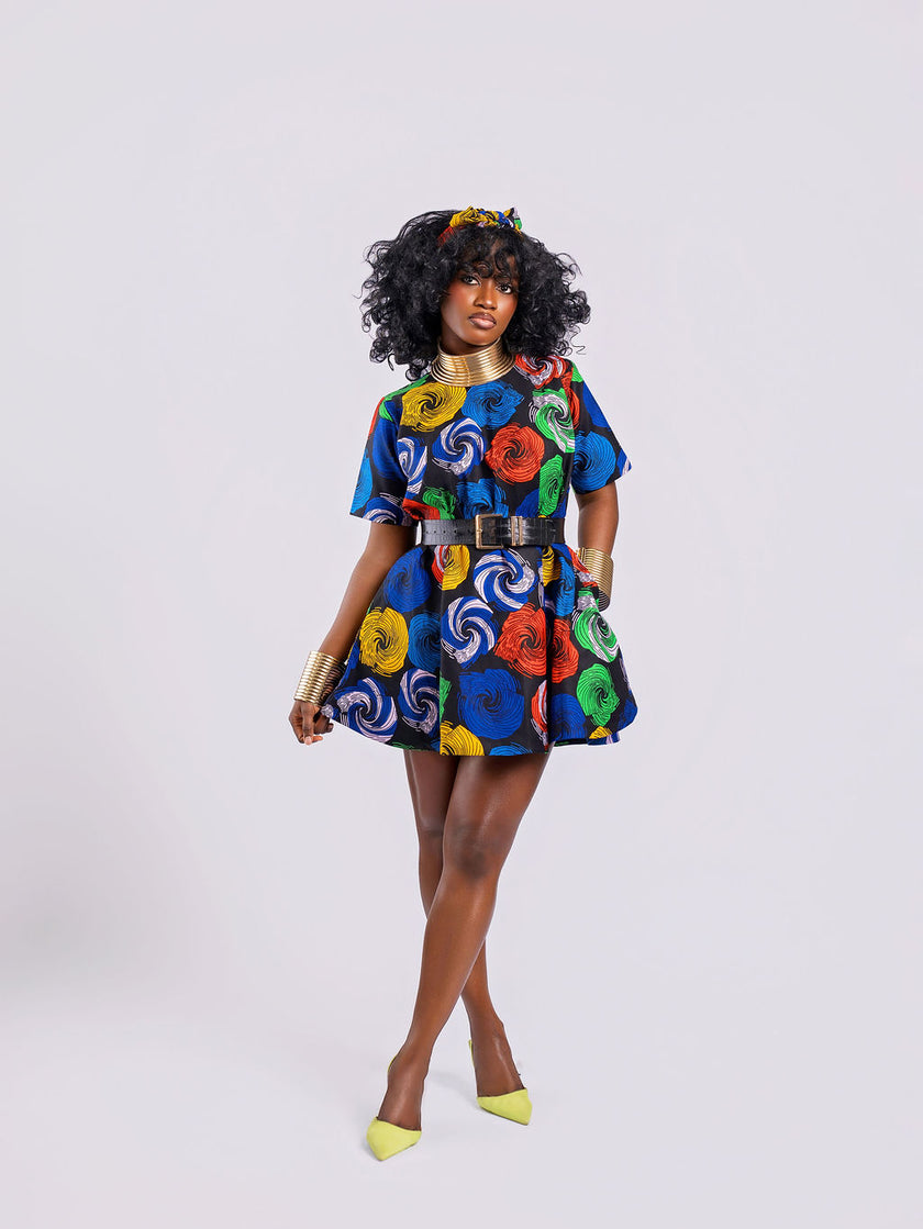 Front view of a model wearing a multi-colored swirl print peplum top with a hand inside one of the two hidden pockets on both sides, styled with a black belt on a white background.