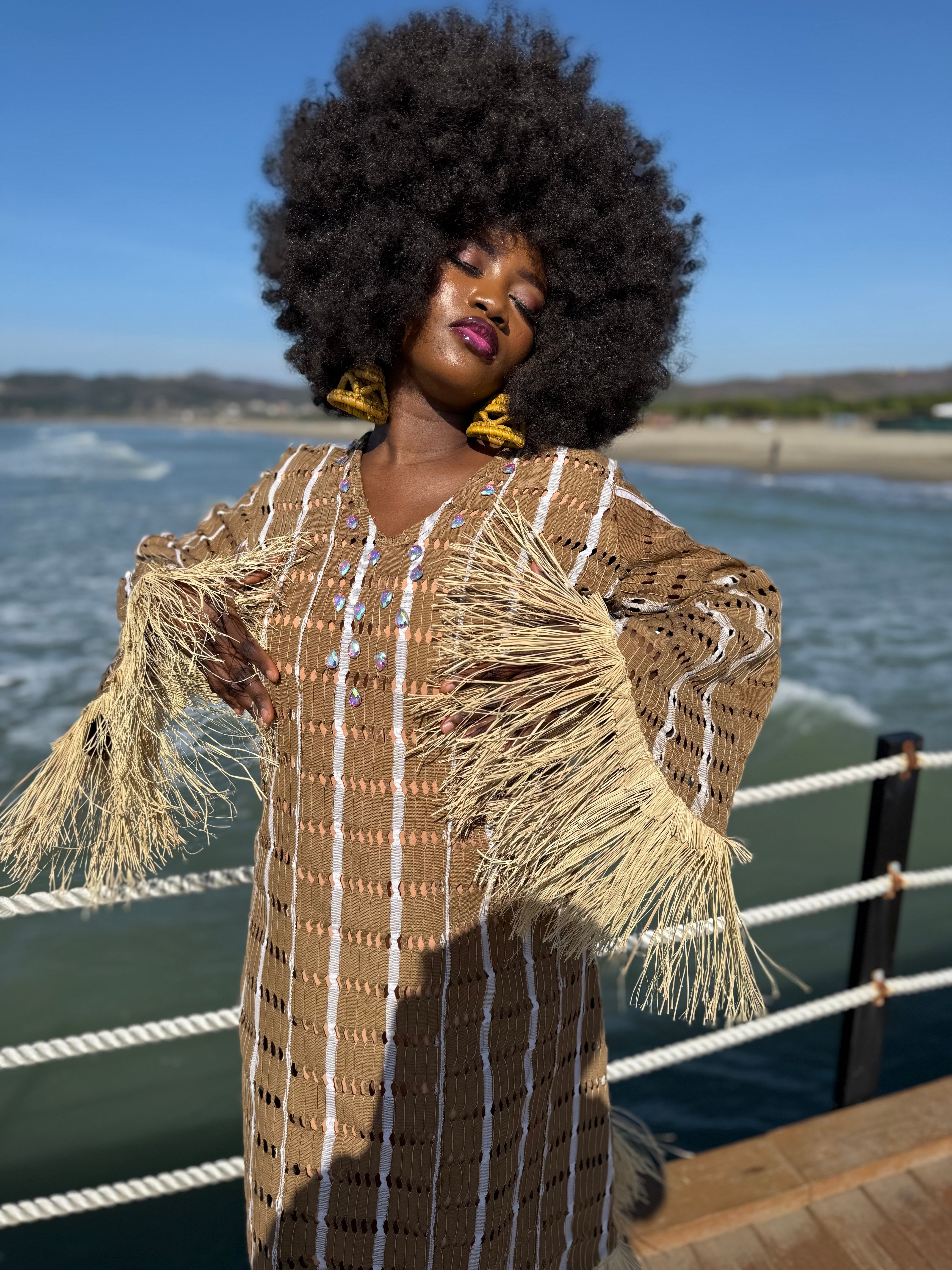 Angle view : Angled view of model wearing the Asàkè dress in natural toned handwoven Aso Oke, highlighting its flowing relaxed fit, raffia accents, and elegant stone details.