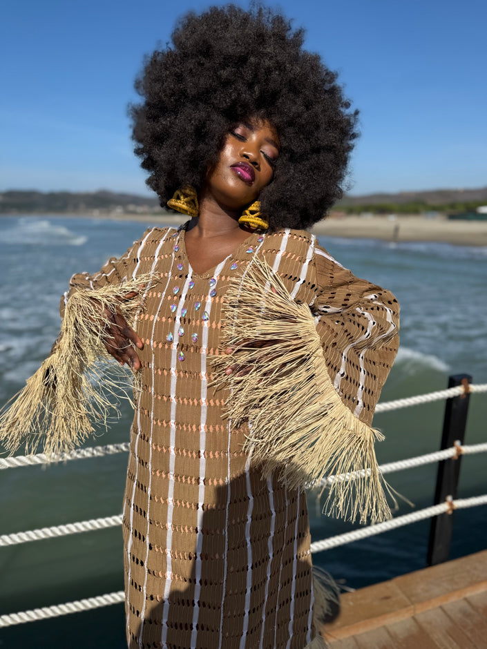 Angle view : Angled view of model wearing the Asàkè dress in natural toned handwoven Aso Oke, highlighting its flowing relaxed fit, raffia accents, and elegant stone details.