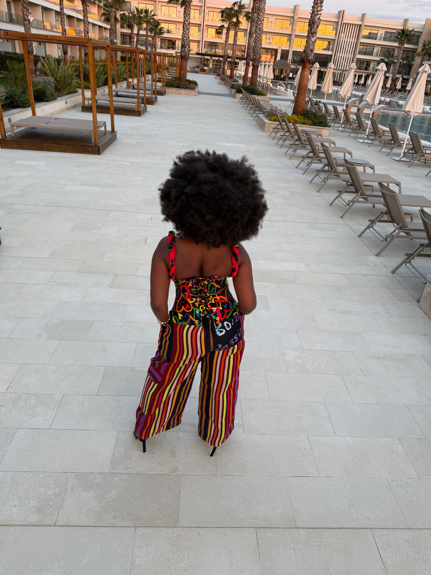 Back view of the Ànìké Ankara corset blouse highlighting the lace-up rope closure, structured boning, and fitted silhouette. The design features braided straps, a sweetheart bustline carried to the back, and vibrant multicolored African print heart-patterned cotton with delicate red lace detailing. This handmade African print bustier top offers adjustable fit, stylish support, and cultural elegance, perfect for weddings, parties, and special events.