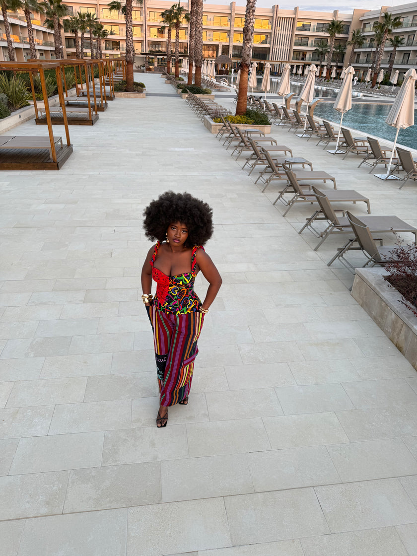 Top view of model wearing the Ànìké Ankara corset blouse, showcasing the sweetheart neckline, braided straps, and structured bustier silhouette. Handmade from vibrant multicolored African print cotton with bold heart patterns and delicate red lace overlay, this corset top highlights the fitted design and elegant detailing, perfect for weddings, cultural celebrations, evening parties, and stylish occasions.