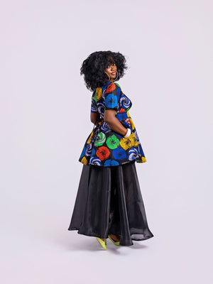 side view of a model wearing The Swirl Peplum & Organdy Set with a hand in the side pocket of the Swirl Peplum.