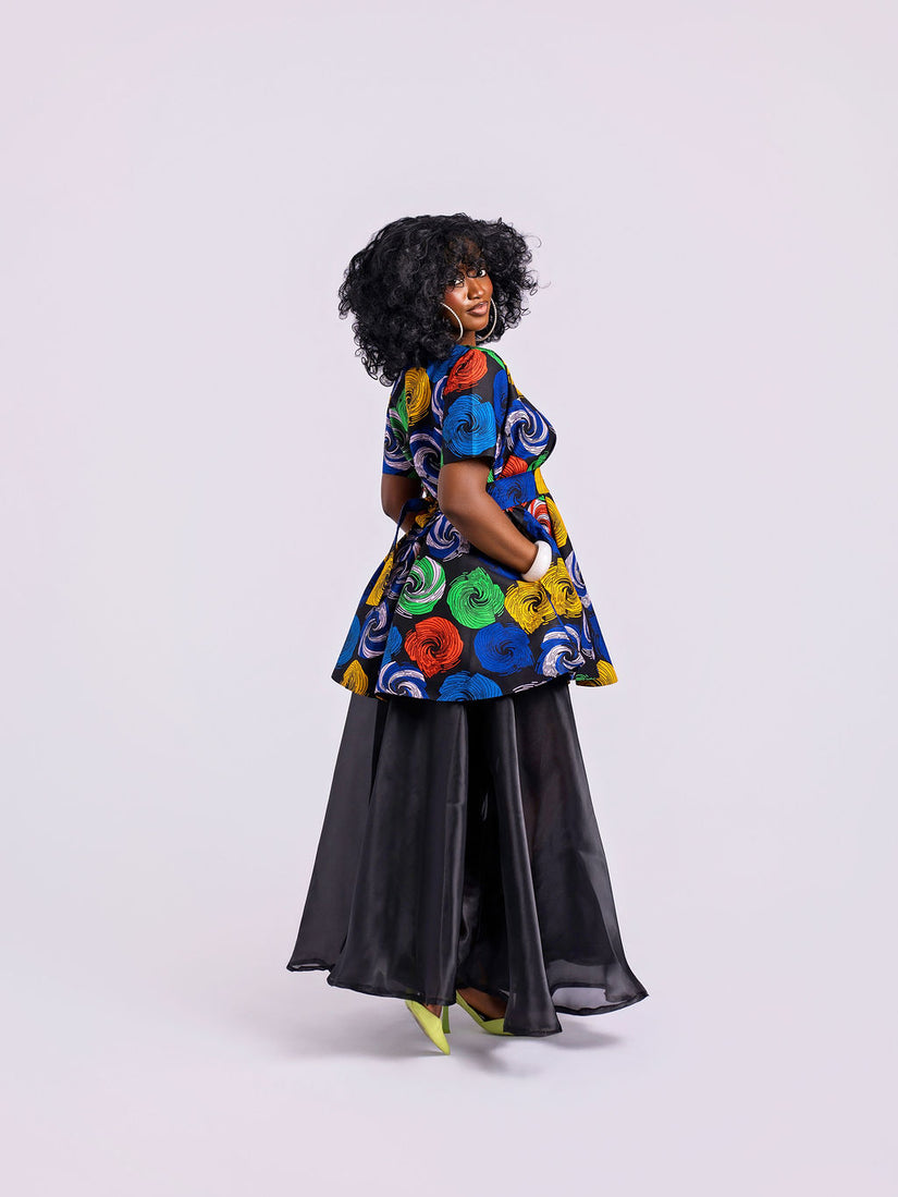 side view of a model wearing The Swirl Peplum & Organdy Set with a hand in the side pocket of the Swirl Peplum.