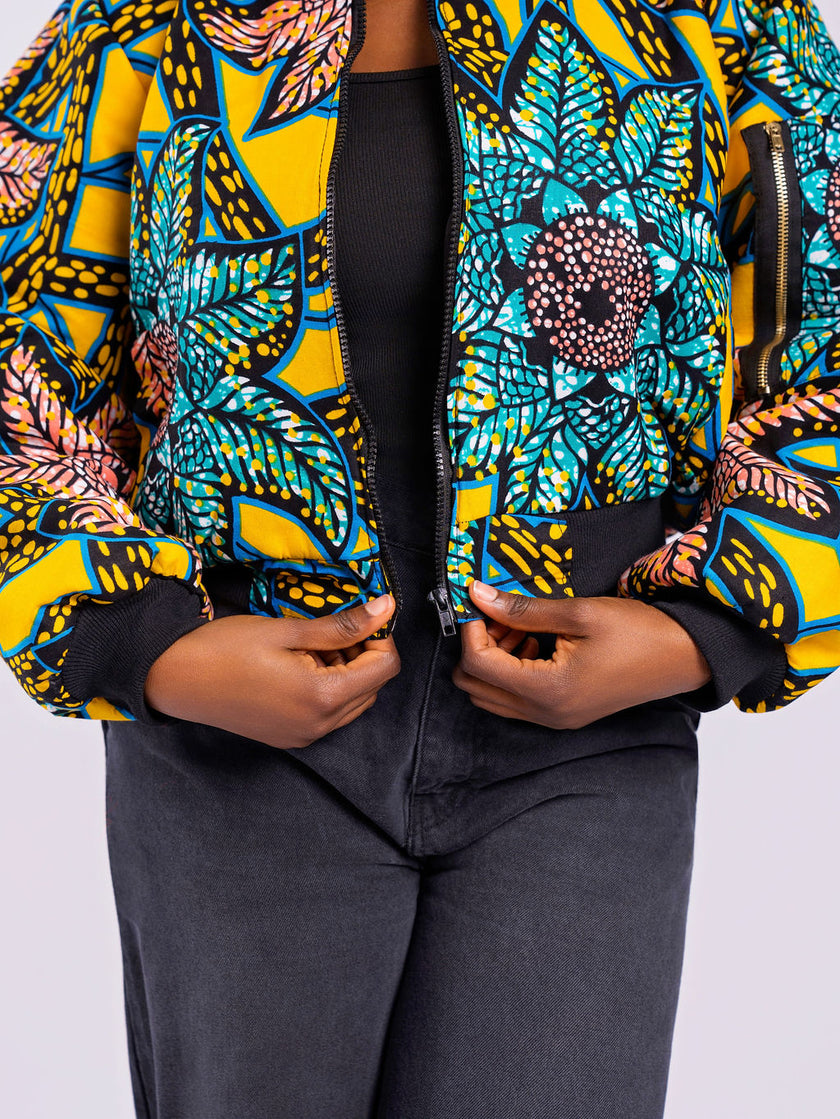 The model wearing a colourful patterned jacket is showing a close-up front view of a cropped bomber jacket styled with high-waisted black jeans.