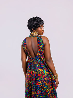 Full-length back view of a woman wearing the Amazin Apparels Kaleidoscope Gown, showing a large circular keyhole cutout and hidden elastic waistband in a vibrant floral African print.