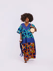front view of a woman in the Amazin Apparels Aso Oke Fusion Gown, featuring a blue pinstripe top with v-neck, bold floral skirt, and floor-length shredded Aso Oke fringe on the sides coming from the waist division made of authentic textured Aso Oke fabric on a multi-patterned maxi dress.