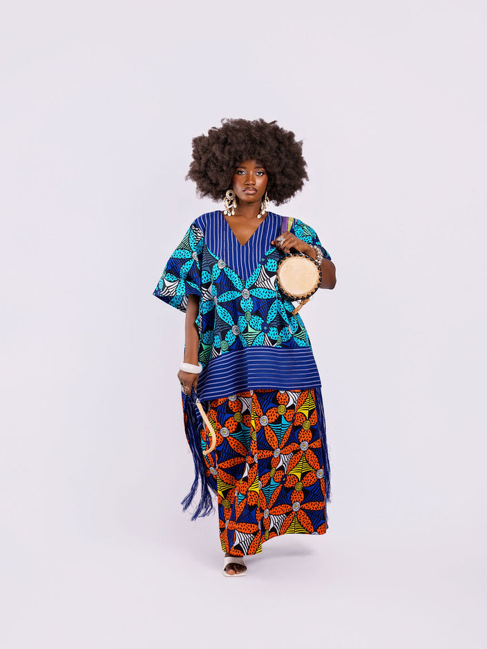 front view of a woman in the Amazin Apparels Aso Oke Fusion Gown, featuring a blue pinstripe top with v-neck, bold floral skirt, and floor-length shredded Aso Oke fringe on the sides coming from the waist division made of authentic textured Aso Oke fabric on a multi-patterned maxi dress.