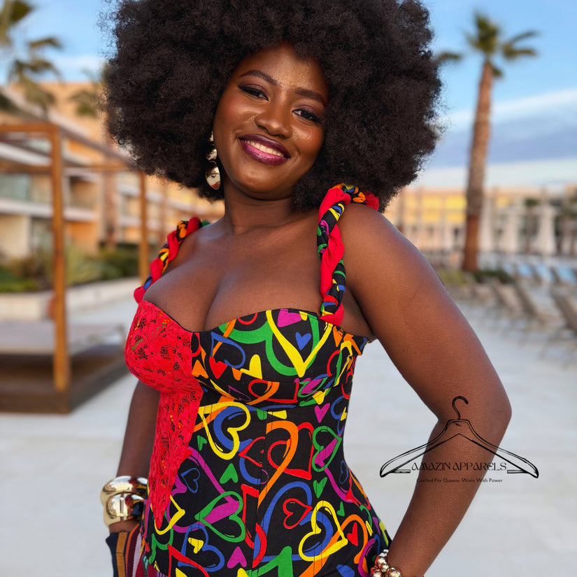 Model wearing the Ànìké Ankara corset blouse featuring a sweetheart neckline, structured boning, padded bust, and lace-up back, designed with vibrant multicoloured African print heart motifs on black cotton and delicate red lace detail. Perfect African print bustier top for weddings, parties, cultural events, and elegant evening occasions.