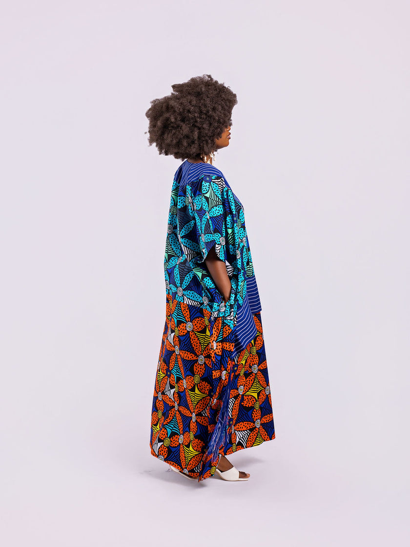 A side view showing the dramatic movement of the blue shredded Aso Oke fringe and the high side slit of the Fusion Gown and A hand tucked into the hidden side-seam pocket, highlighting functional design.
